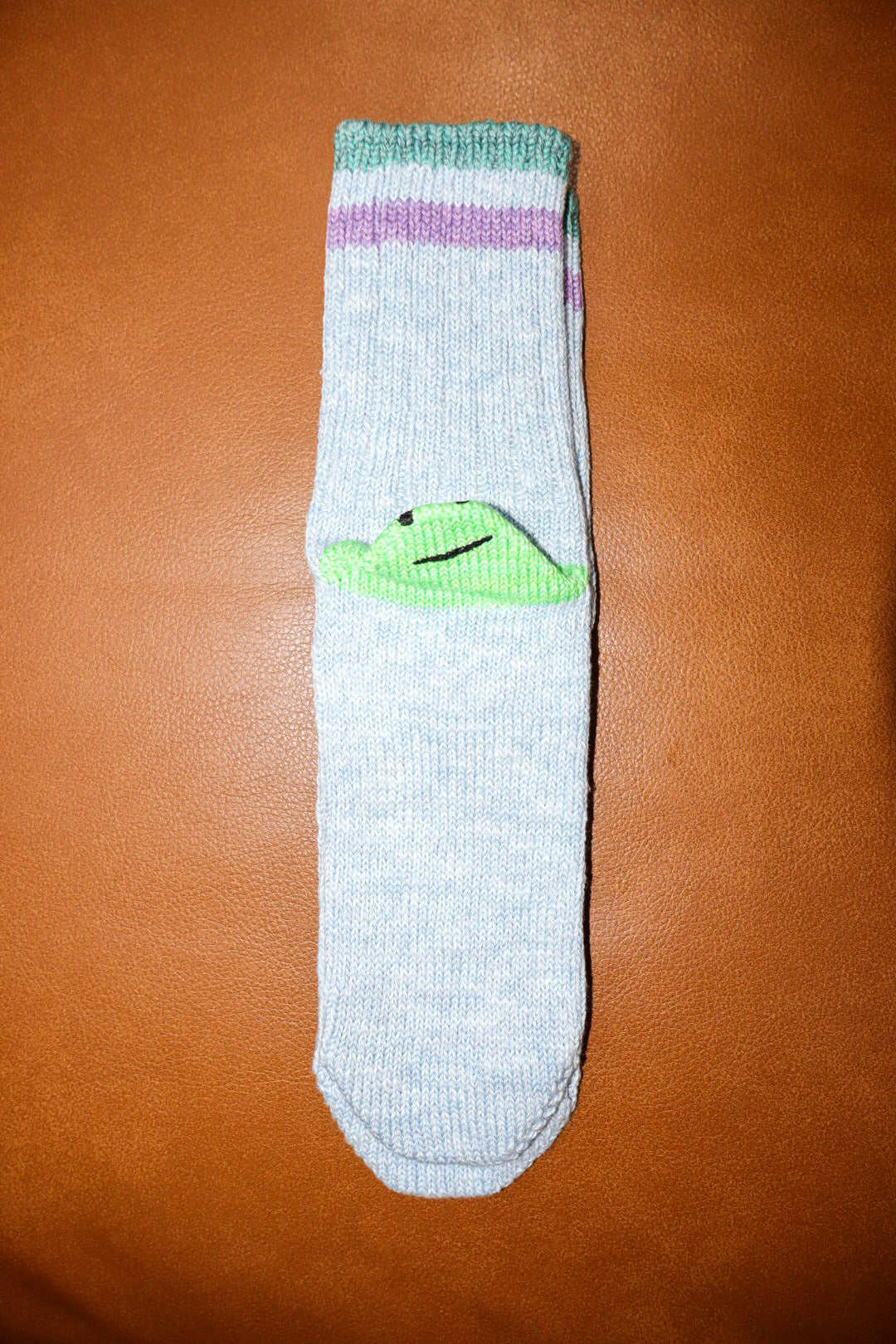 Light green sock with green paw print on a brown surface