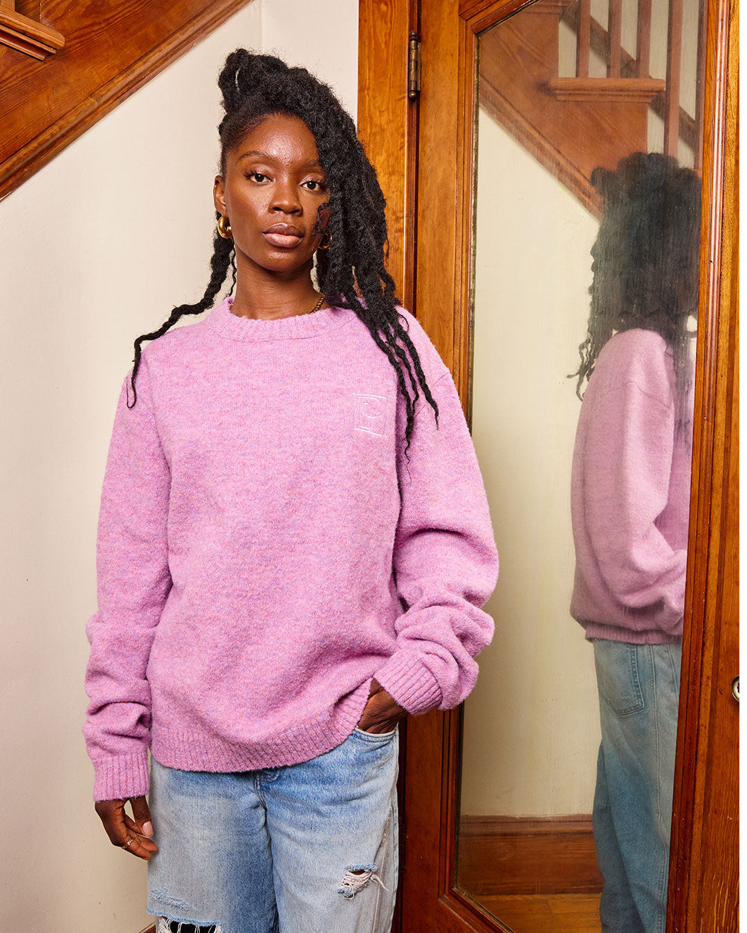 Woman wearing a pink sweater and light blue jeans standing in front of a mirror.