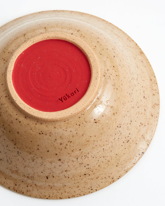 Ceramic bowl with red interior and speckled beige exterior on a white background