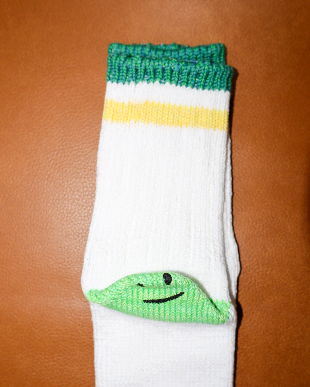 White sock with green top and smiley face design on a brown surface
