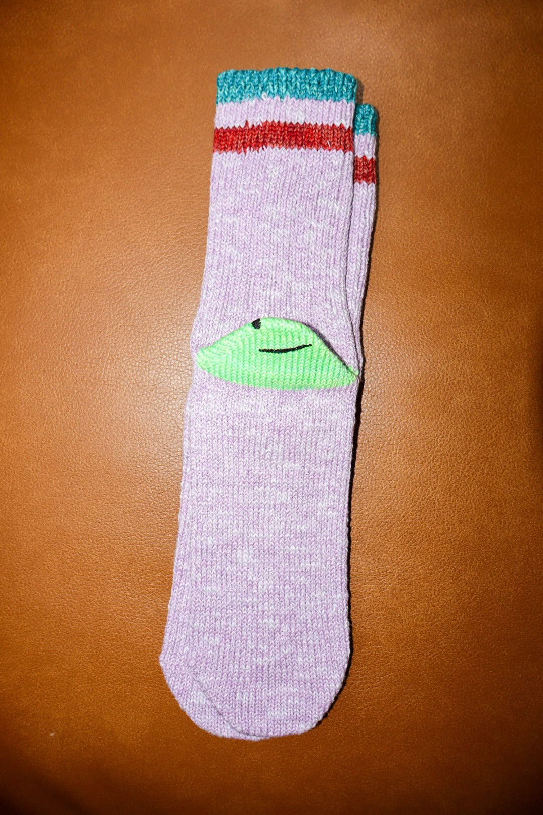 Gray sock with colorful top and green heel on a brown surface
