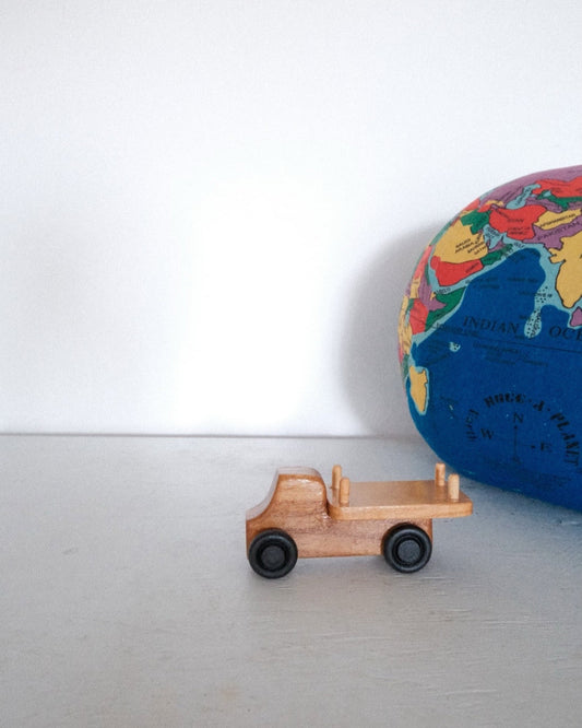A handmade wooden toy car placed on a shelf next to a globe, displaying its side profile.