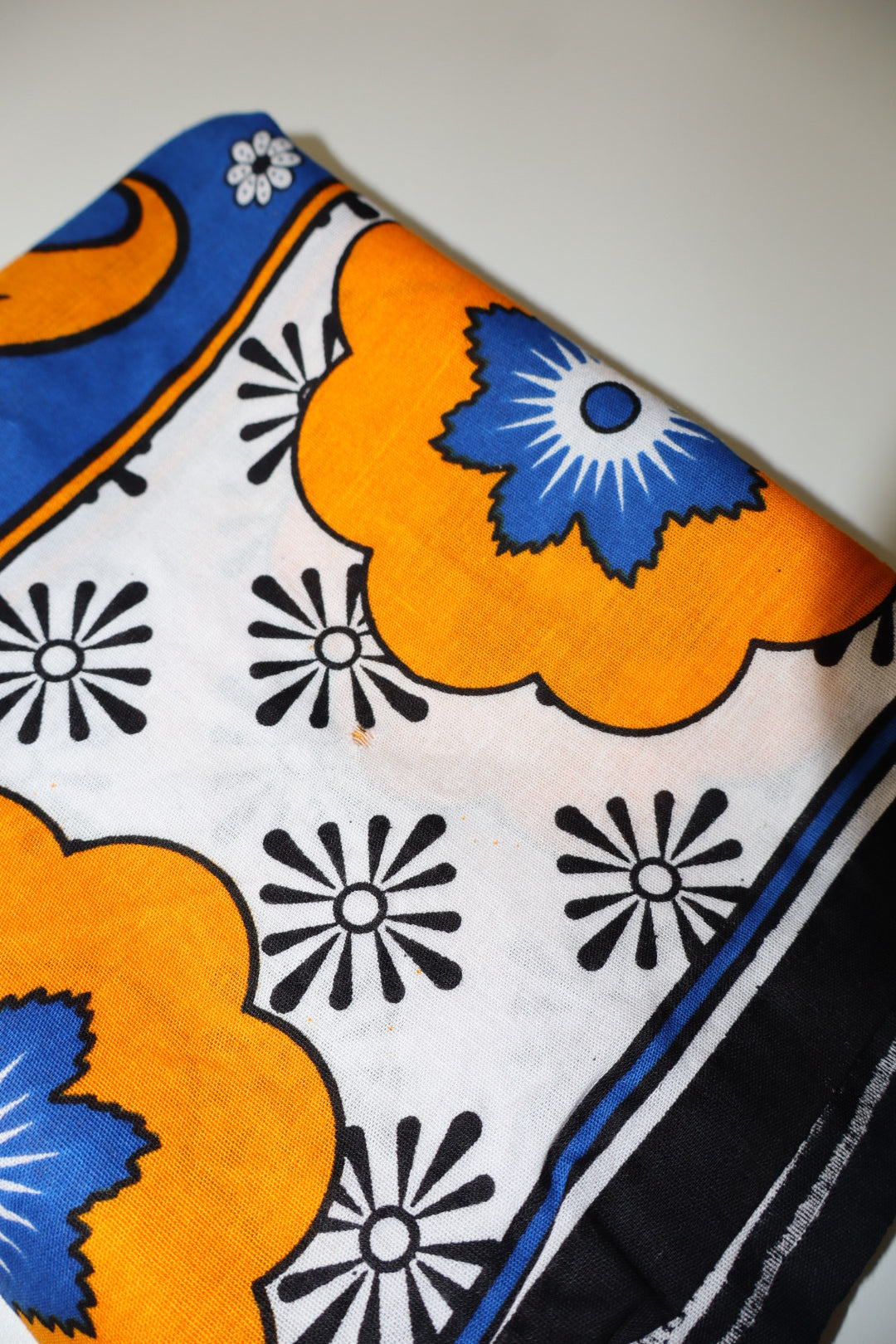 Close-up of a fabric with orange, blue, and black floral patterns on a white background.