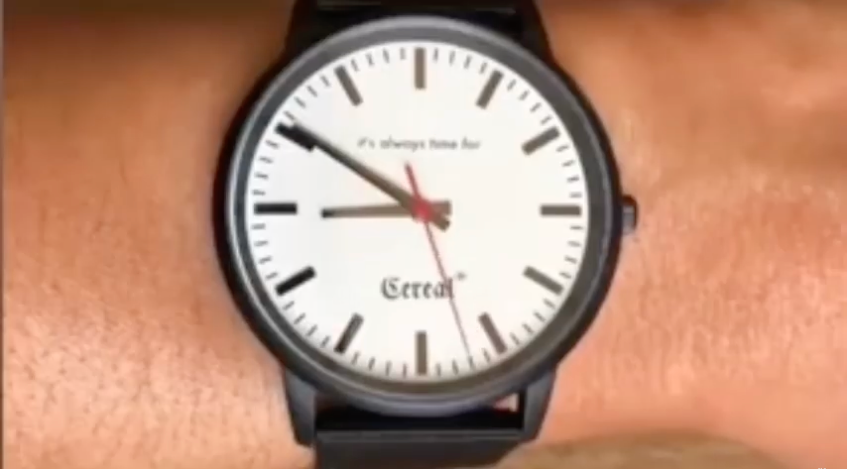 Wrist wearing a watch with a white face and black strap.