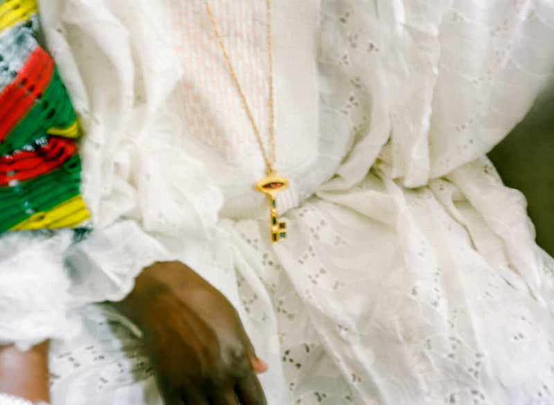 Close-up of a person wearing a gold necklace with a pendant, surrounded by colorful fabric.