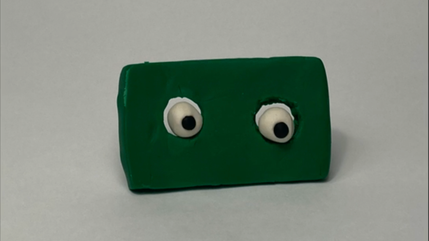 Green rectangular object with googly eyes on a gray background