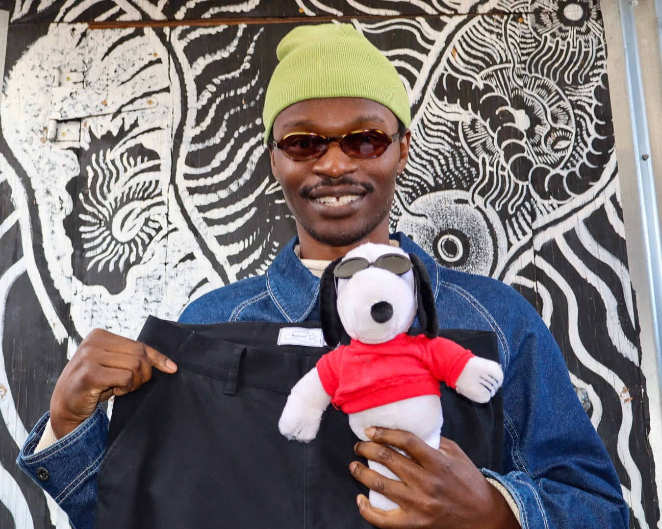Person holding a black jacket and a plush toy with a red shirt against a patterned wall.