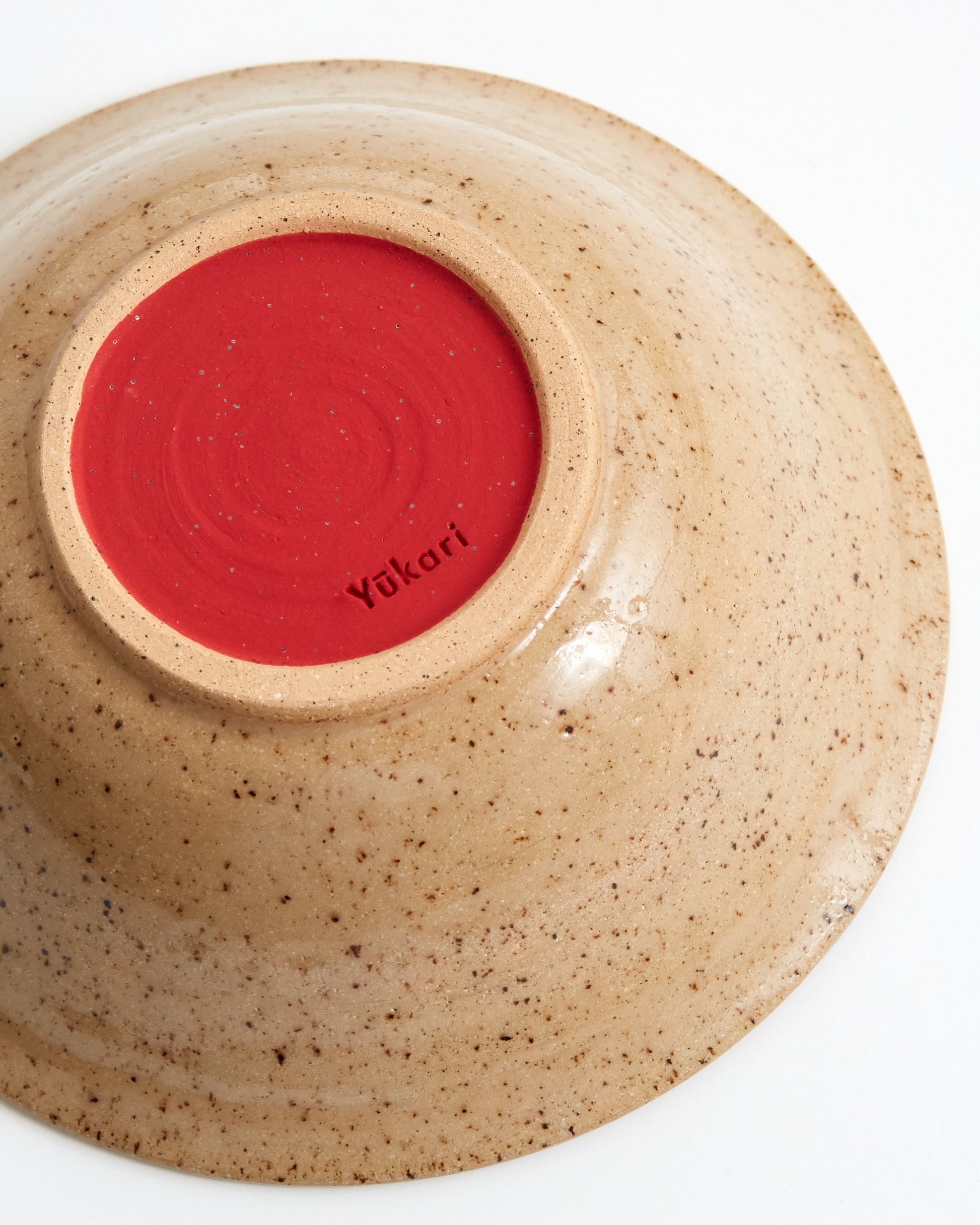 Ceramic bowl with red interior and speckled beige exterior on a white background
