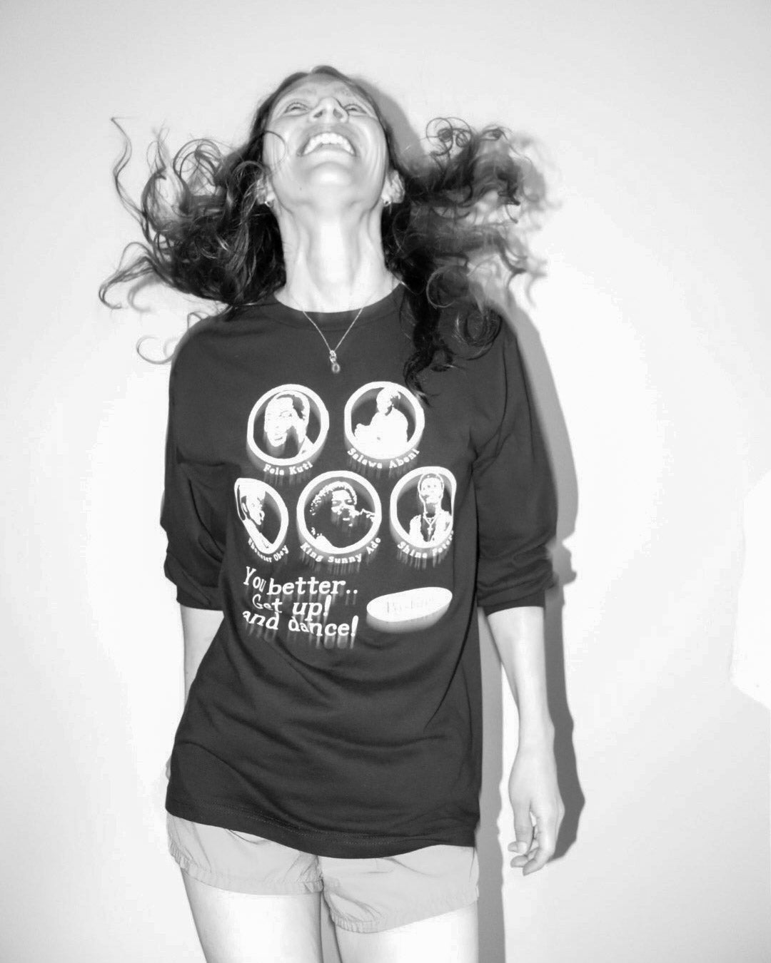 A woman wearing a black graphic t-shirt with white printed images and text, captured in a high-contrast black and white photo against a plain background.