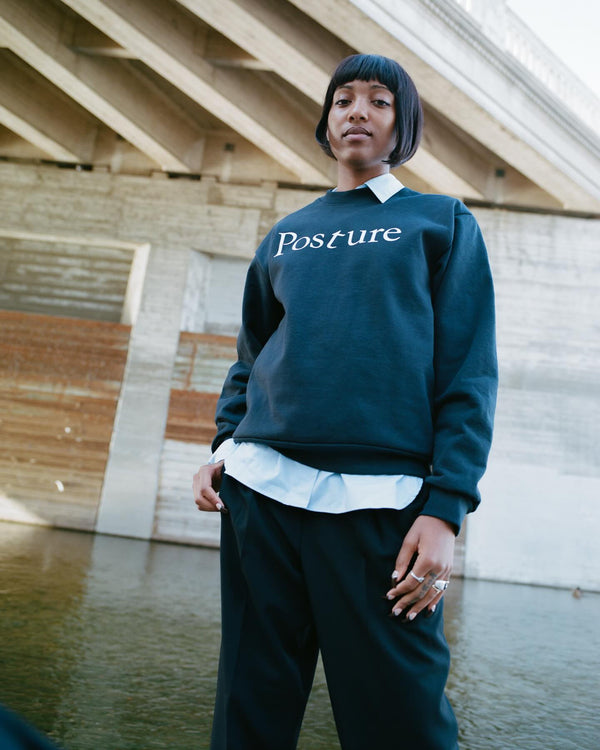 Person wearing a dark green sweatshirt with 'Posture' text, standing by a body of water.