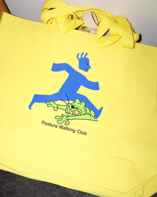 A bright yellow canvas tote bag with a blue and green graphic of a person walking over a cartoon creature, with the text 'Posture Walking Club' printed below.